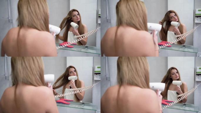 年轻女子在浴室里用吹风机吹干头发时照镜子。