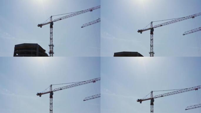 塔式起重机背光的鸟瞰图在建筑工地工作。晴天飞越建筑开发。无人机从底部上升到顶部