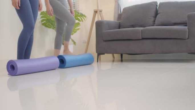 两名亚洲妇女在客厅里散布瑜伽垫进行放松锻炼。用脚铺垫子。热爱健康的人。健康的生活方式理念。