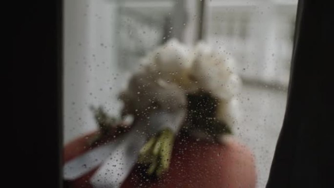 一束白色牡丹系着的白色丝带躺在玻璃后面，上面有雨滴。
