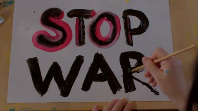在纸上画一幅停止战争海报。孩子的手握着刷子，写了一封信。