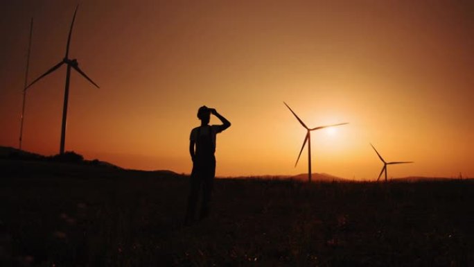 剪影非裔美国人在夏季日落时站在大风车上。环境污染的概念，替代能源的新技术。风车的背景