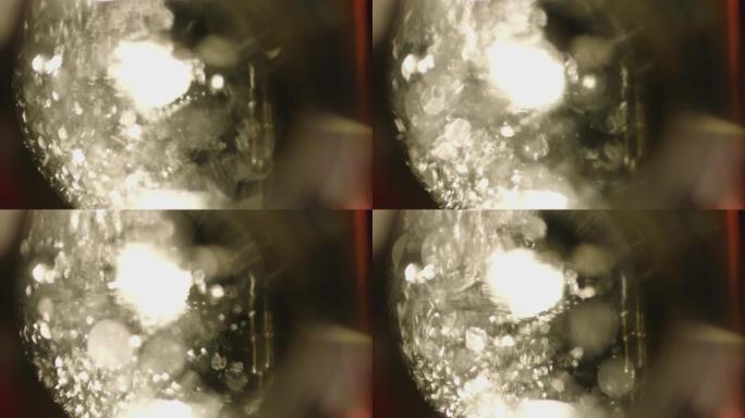 4k沸水倒入黑色背景的玻璃中。抽象散焦晶体元素。在玻璃下近距离拍摄。许多晶体从上面落下。散焦特写