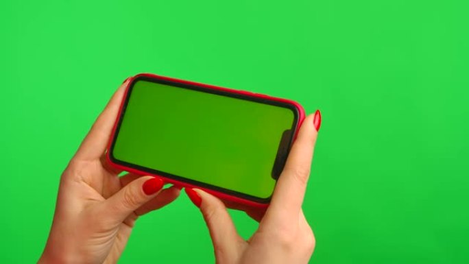女性手持水平位置的绿色背景上带有工作区模拟屏幕的手机。女人在互联网上浏览内容。广告区域。文本或图像的