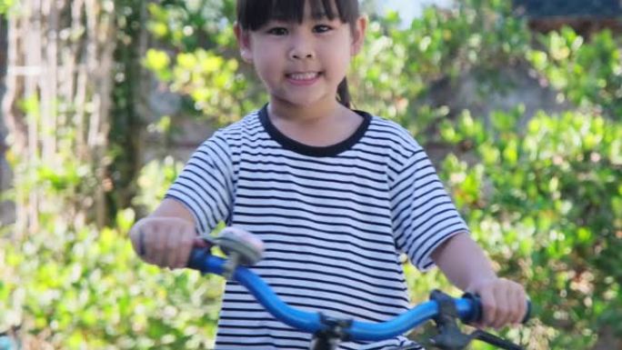 开朗的微笑女孩在自行车车把上敲响自行车铃，准备在公园里骑自行车。