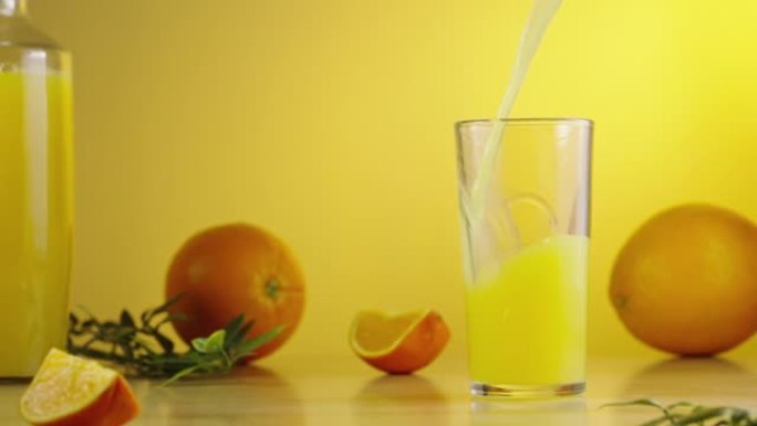 将鲜榨的甜橙汁倒入玻璃杯中。早上早餐的黄色厨房背景。玻璃中的异国天然柑橘花蜜。饮食健康热带饮料。慢动