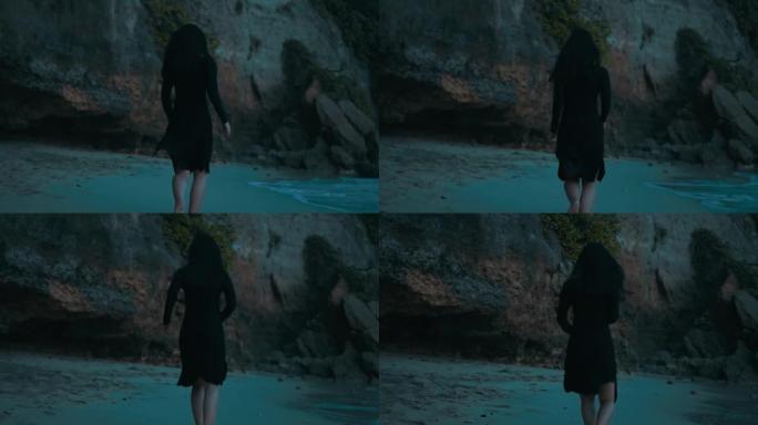 下午穿着黑色连衣裙在沙滩上奔跑并摔倒的女人