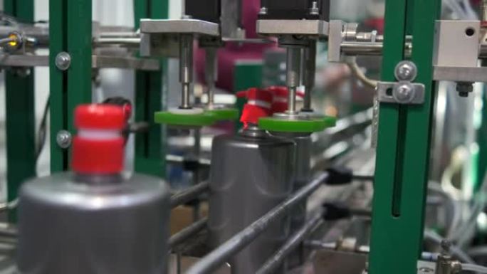 为家庭生产洗涤剂的企业。机器将带有分配器的红色塞子拧到装有液体的灰色塑料瓶上。输送线。