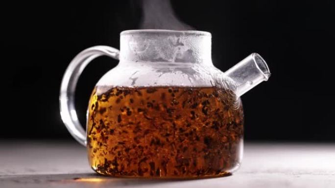 在深色背景下的玻璃透明茶壶中酿造红茶的过程。将热水倒入带茶叶的水壶中。