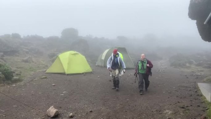 一位白人男性游客带着他的黑色向导走到Baranco营地。攀登乞力马扎罗山