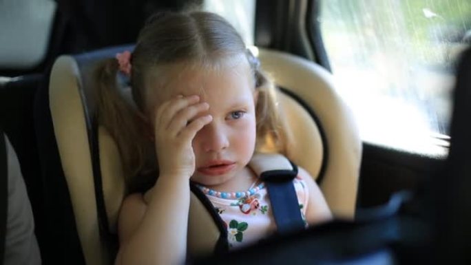 两岁的女孩坐在儿童汽车座椅上的汽车上。哭泣和非常沮丧。