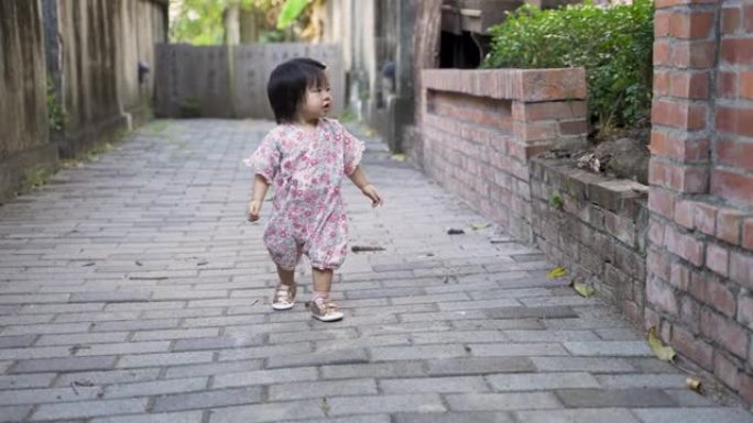 穿着和服的好奇的亚洲女性蹒跚学步的孩子正停下来看着远处，一边快乐地奔向镜头