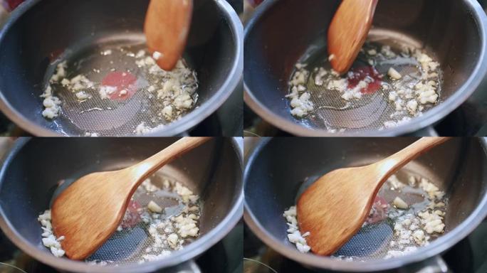 关闭木勺在煎锅热煎锅中搅拌嘶嘶作响的大蒜油