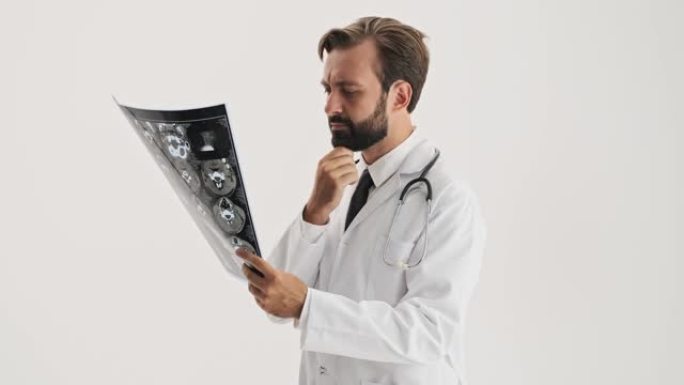 认真的男人医生，听诊器思考并抚摸胡须，同时专心观察x射线图像