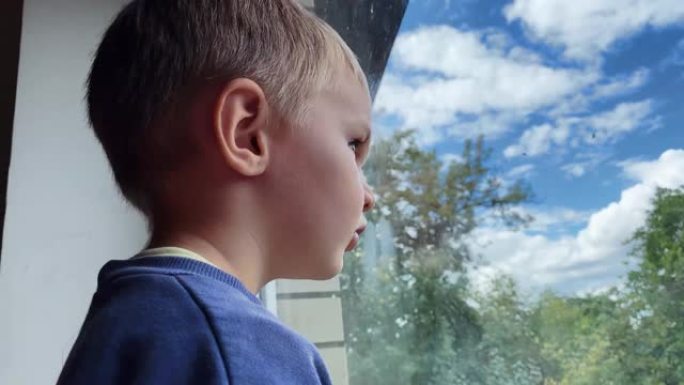 小高加索男孩看着窗外，然后在夏天的一所私人住宅里对着镜头微笑