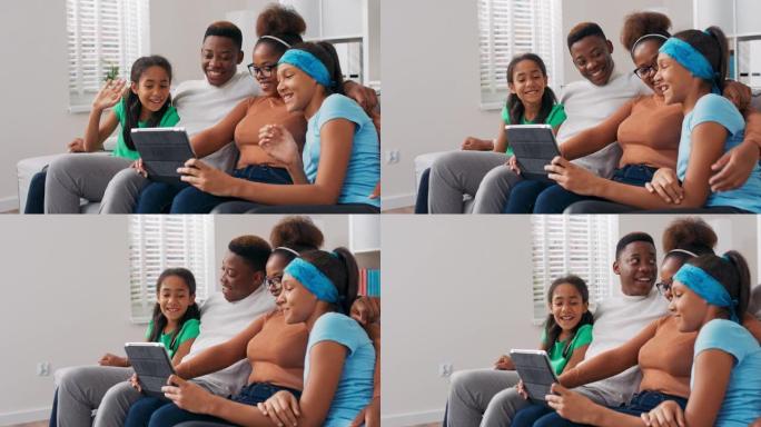 一个幸福的家庭坐在沙发上，放松身心，下午一起度过时光，父母带着两个女儿在平板电脑上挥手，与朋友进行视