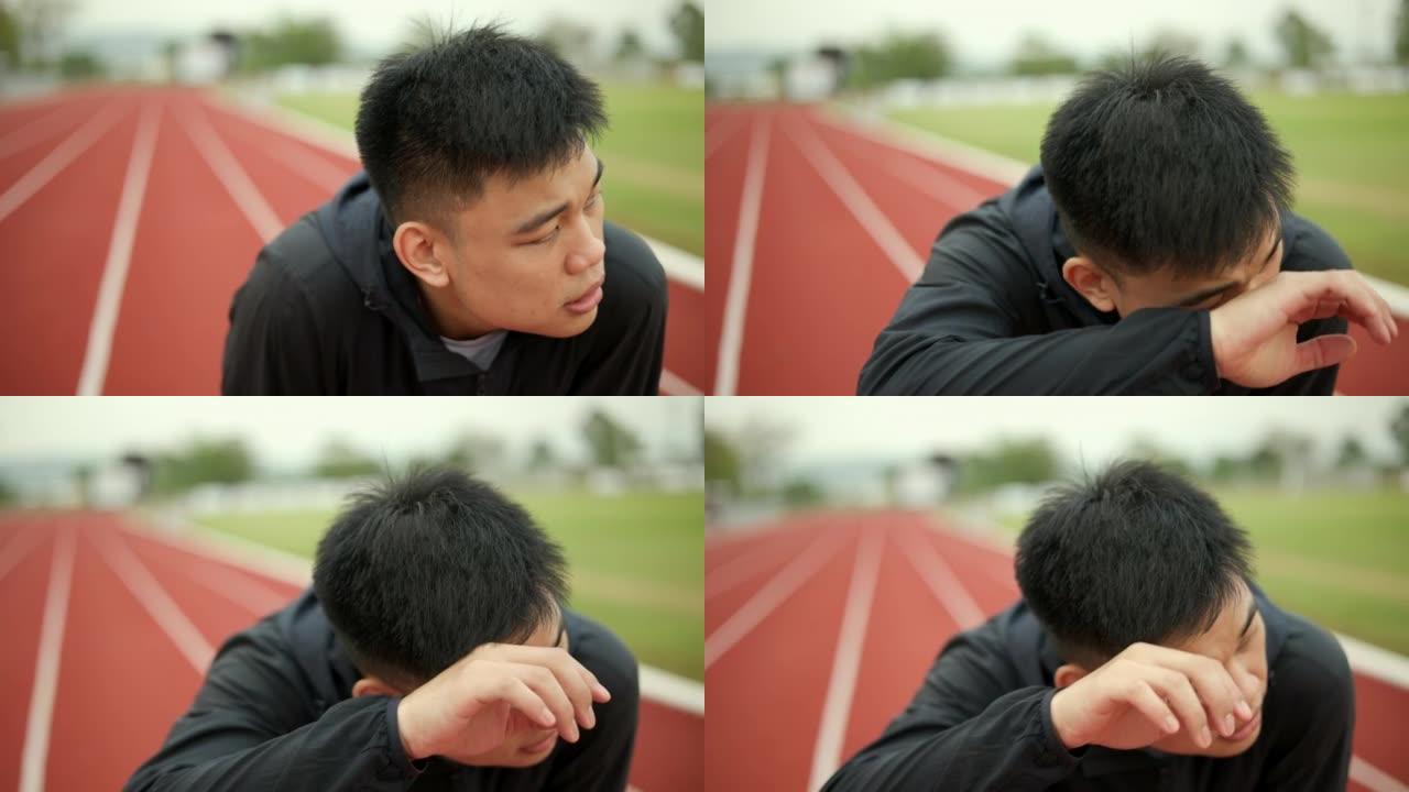 中国年轻人在体育馆的跑道上慢跑时累了。年轻的亚洲男性激烈训练锻炼挑战呼吸疲惫。健康积极的生活方式理念