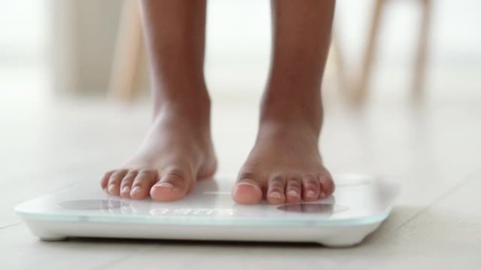 黑人女孩站在秤上测量体重的腿。非裔美国女性赤脚在家用体重秤。节食、控制和测量