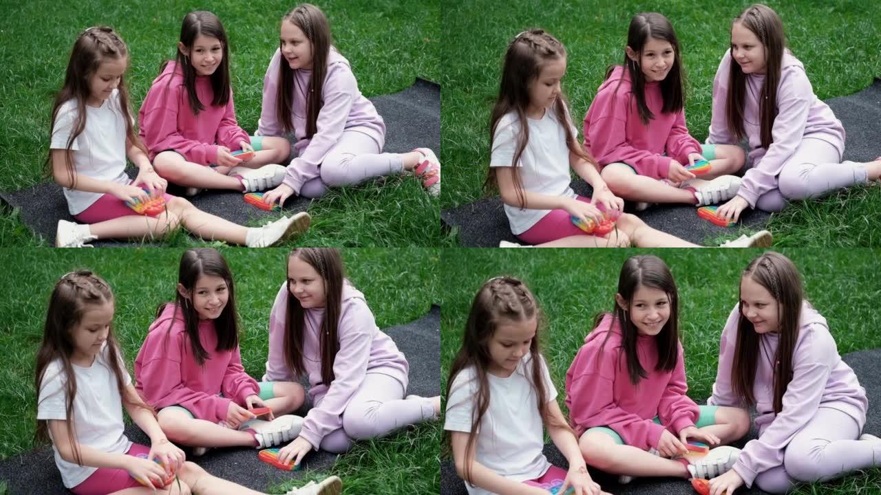 3个女孩在户外草地上玩时髦的感官玩具。推流行泡泡柔性烦躁感觉玩具。压力和焦虑缓解。压力儿童和成人的硅