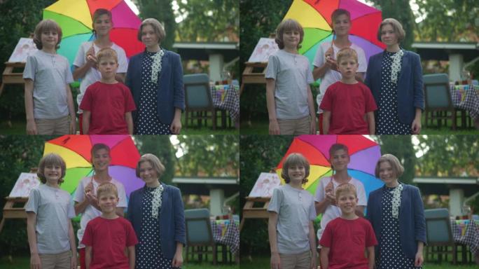 中等镜头正面的高加索男孩和女孩看着相机微笑着旋转彩色雨伞站在户外。快乐的朋友在春夏后院慢动作摆姿势。