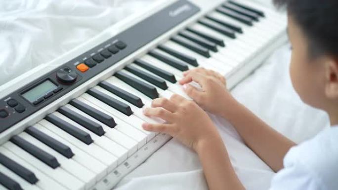 亚洲人和他的狗在床上练习钢琴和电子