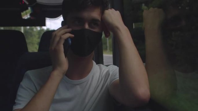 男子在公共交通巴士上打电话。脸上有一个面具。