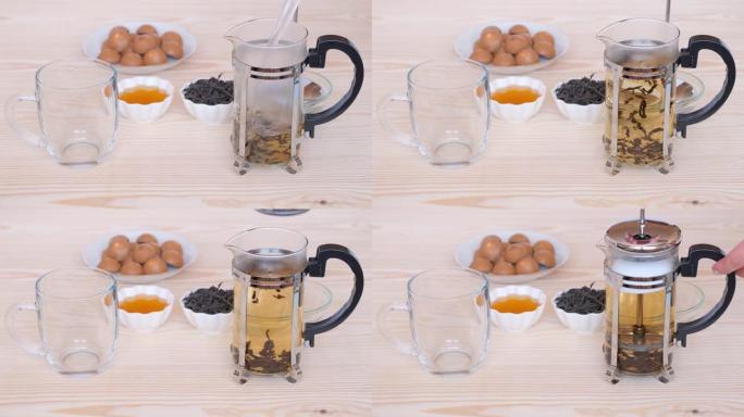 在玻璃法式咖啡中冲泡红茶-在木桌的背景上压榨，并带有杯子，用于茶，蜂蜜和糖果。