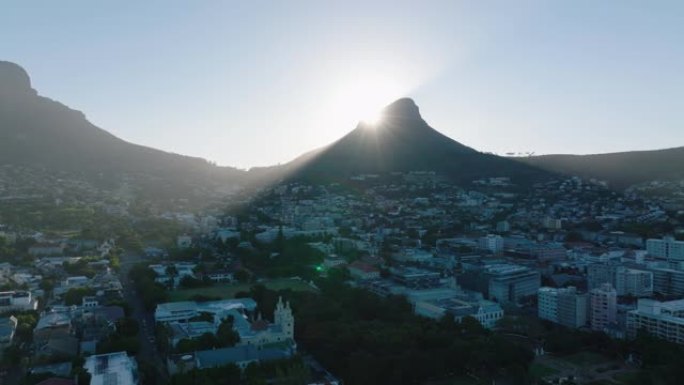 升起的太阳在住宅区上方的高峰后面。狮子头山在镇上投下阴影。南非开普敦