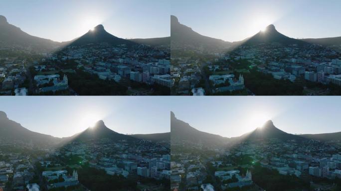 升起的太阳在住宅区上方的高峰后面。狮子头山在镇上投下阴影。南非开普敦