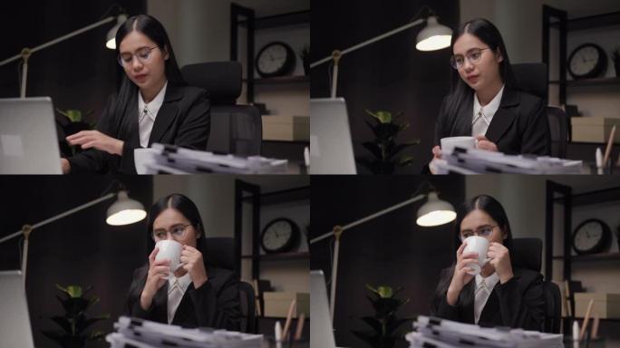 聪明的女商人在夜间办公室喝咖啡，看电脑显示器。她如此认真地检查晚上在笔记本电脑加班的工作任务