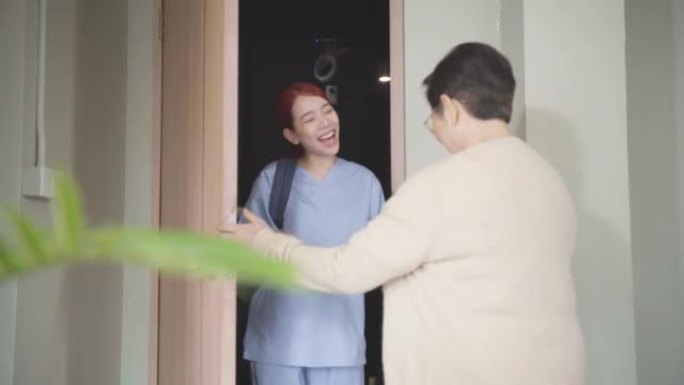 亚洲女性护士穿着磨砂膏，家庭护理人员在入口处挥手交谈，拜访亚洲高级女性。家庭保健和疗养院概念。慢动作