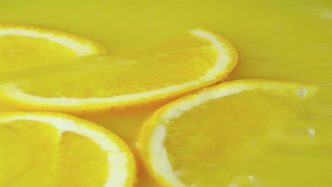 黄色橙汁配橙子水果两半。关闭柑橘异国甜花蜜，橙色切片在液体中旋转。早餐用热带鲜榨饮料的背景。慢动作