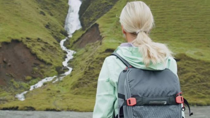在冰岛南部海岸Fjadrargljufur附近的冰岛瀑布前背着背包的女游客