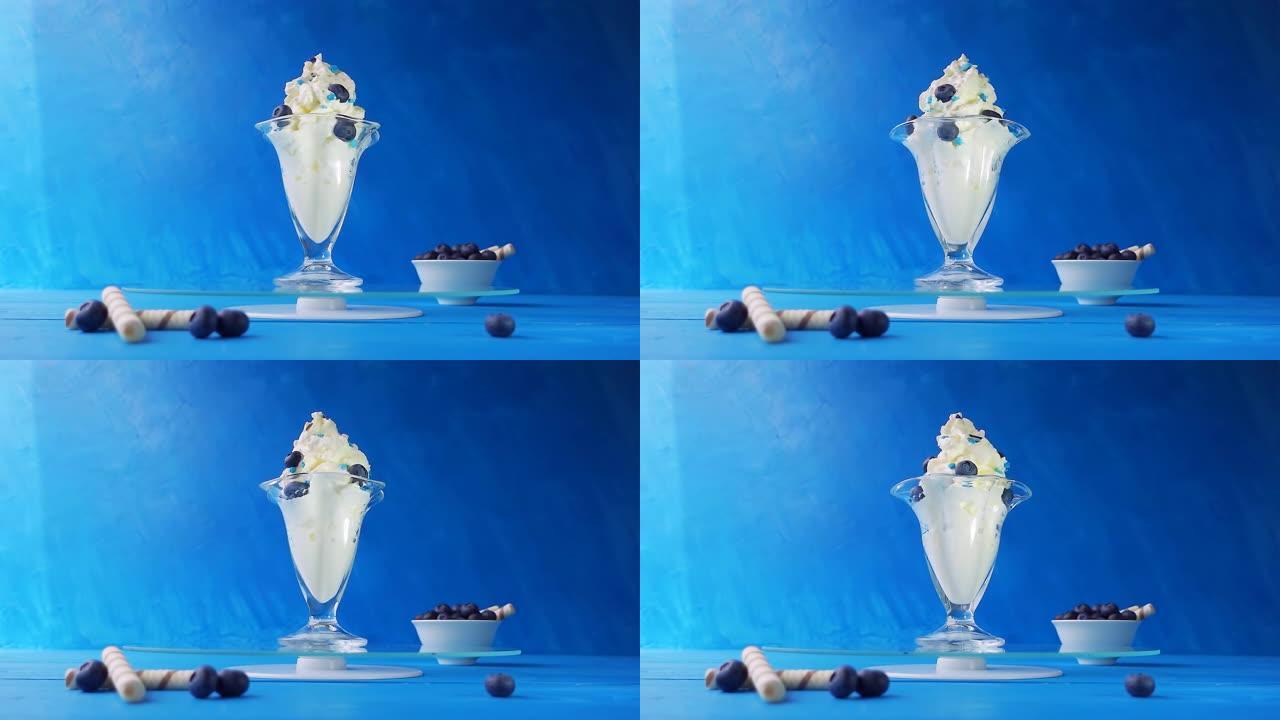 蓝色背景的木制桌子上的托盘上的玻璃旋转蓝莓冰淇淋。具有速度斜坡效果的创意慢动作4k循环视频。