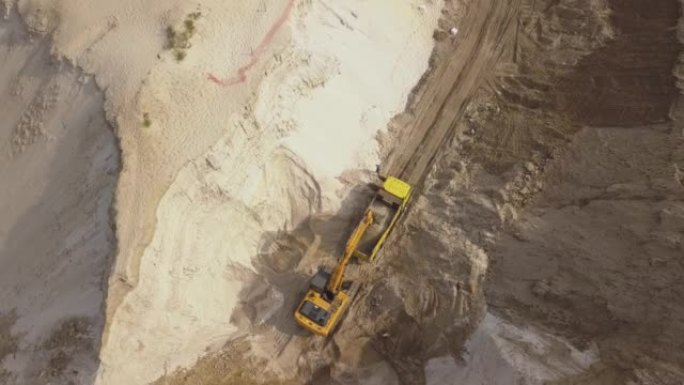 挖掘机将沙子装入自卸车。采矿卡车运输采砂场中的矿物。露天采矿的鸟瞰图。