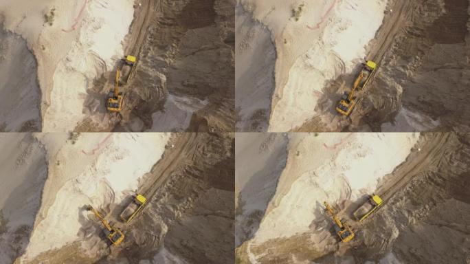 挖掘机将沙子装入自卸车。采矿卡车运输采砂场中的矿物。露天采矿的鸟瞰图。