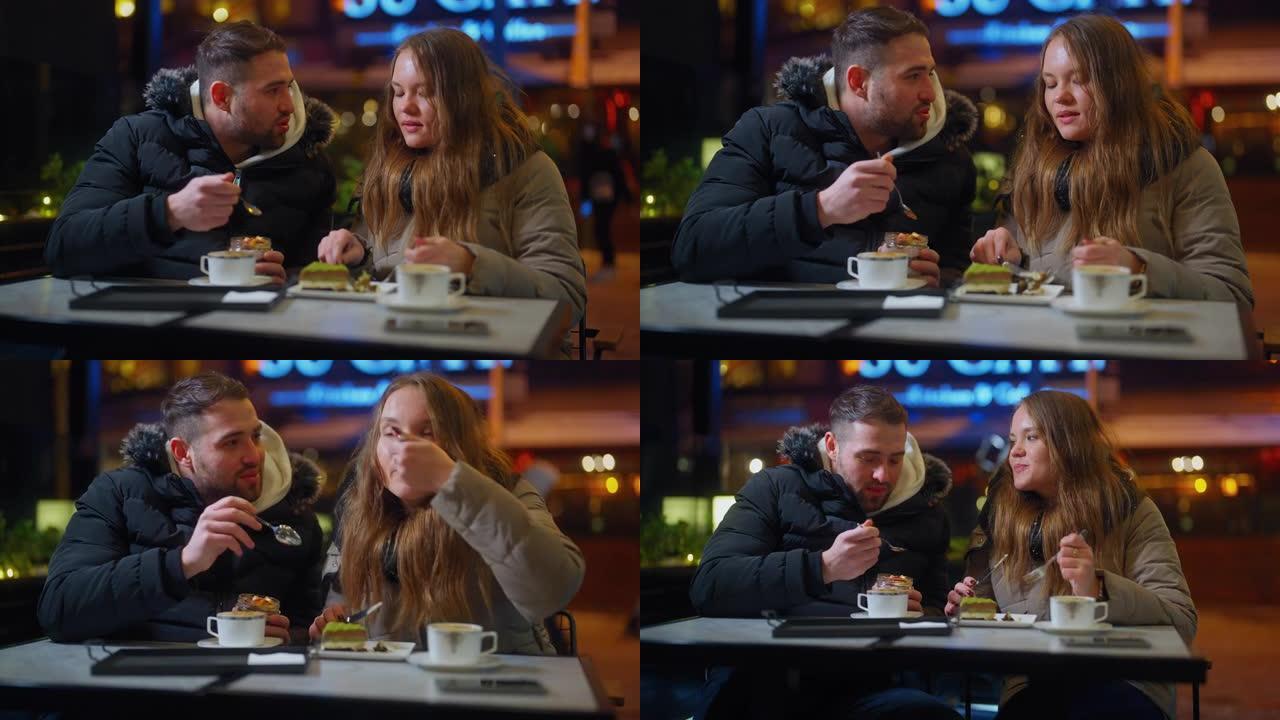 年轻夫妇在咖啡馆约会，晚上在城市的冬天一起享受热饮和甜食