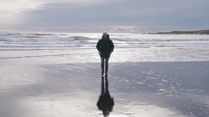 男子沿着阳光普照的湿海滩走向相机