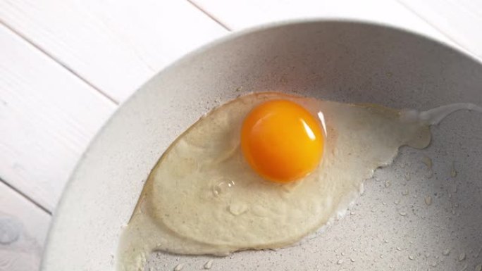 破解蛋壳并在慢动作的煎锅中烹饪阳光充足的侧面鸡蛋