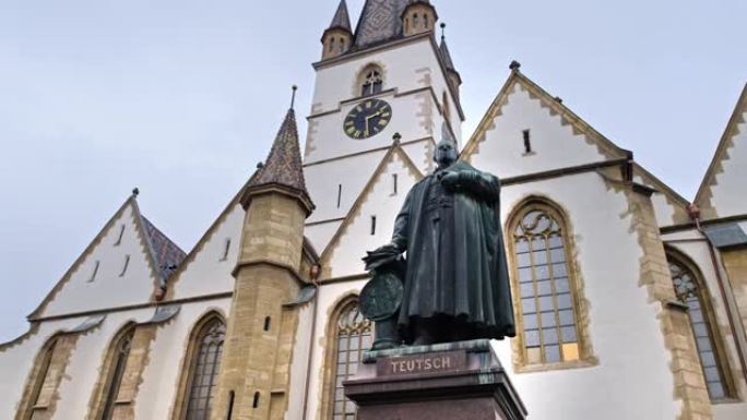 罗马尼亚锡比乌的乔治·丹尼尔·特伊施主教雕像。背景上的锡比乌·路德教会大教堂