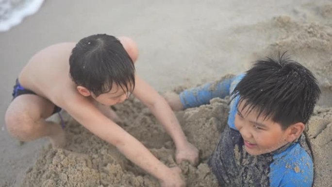 亚洲男孩兄弟在日落时在海滩上享受和玩海和沙子