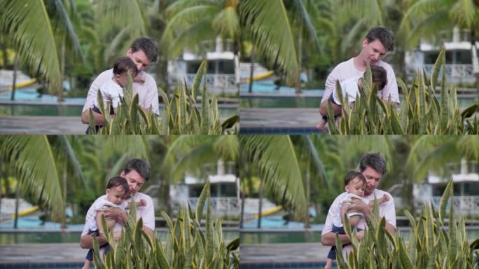 有孩子度假的假期。绿色的花朵旁边站着一个年轻的父亲和儿子。婴儿大约10个月大。孩子俯身向美丽的绿色花