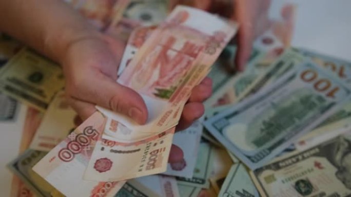 一堆钱俄罗斯卢布和美元，男性手选择5000张俄罗斯钞票，并把它们放在一个包里。