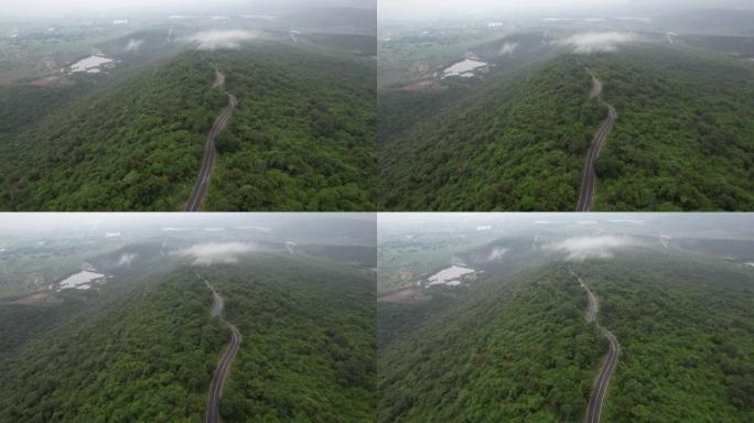 空中无人机电影拍摄的汽车和道路在早上下雨后越过山顶，有雾和绿色森林。