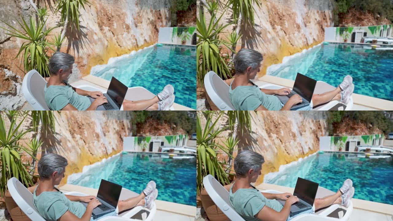 在度假酒店度假期间，放松成年男子在游泳池边放松，在笔记本电脑空屏幕上观看新闻或视频
