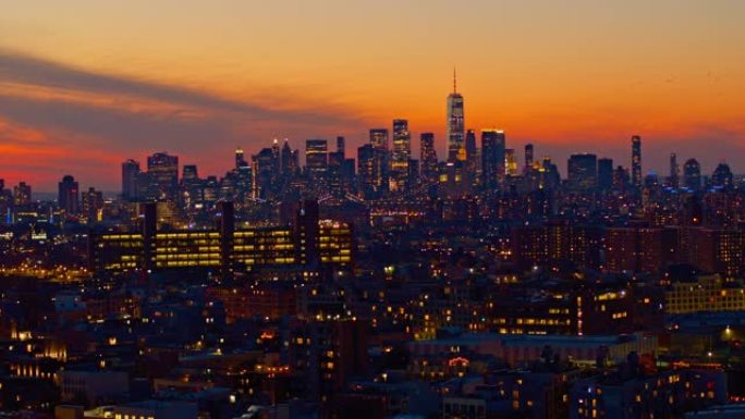 鸟儿在曼哈顿市中心戏剧性的天空中飞行，自由塔在夜晚照亮。日落时分，可以看到布鲁克林住宅区的远景。静态