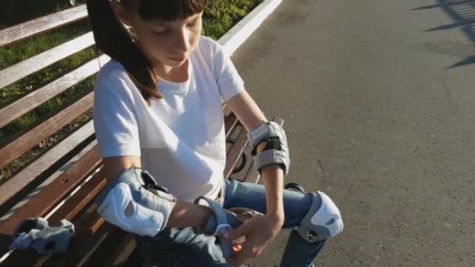 一个穿着白色t恤和牛仔裤的女孩穿着滚轮和手脚保护装置，打算在公园里骑车。