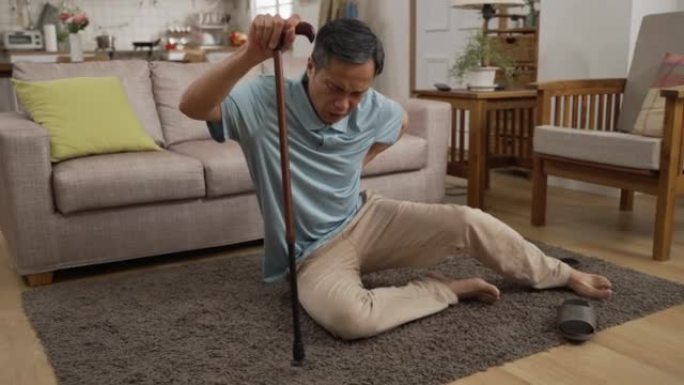 亚洲老人滑倒并摔倒在家里客厅的地板上后，试图慢慢起床。当用棍子支撑自己时，他感到下背部非常疼痛
