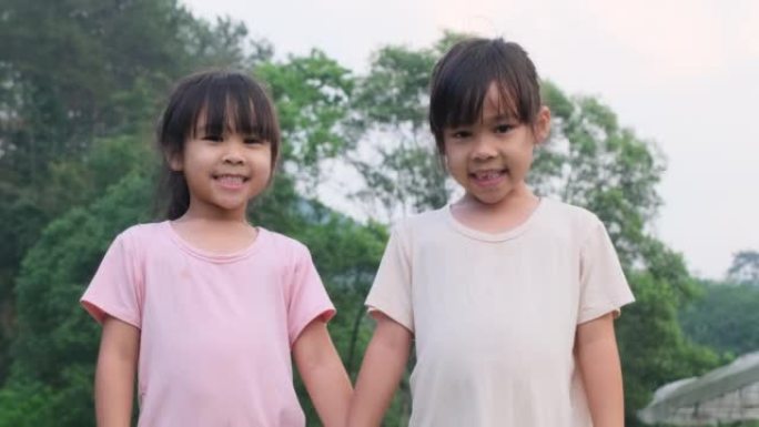 两个可爱的亚洲姐妹手牵着手站在夏天的花园里。两个可爱的小女孩在公园里微笑和玩耍的肖像。