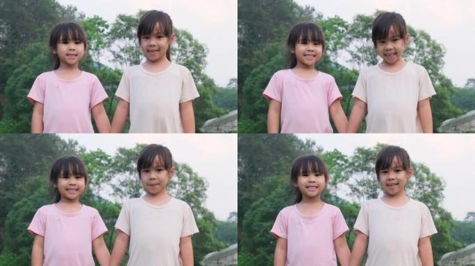 两个可爱的亚洲姐妹手牵着手站在夏天的花园里。两个可爱的小女孩在公园里微笑和玩耍的肖像。